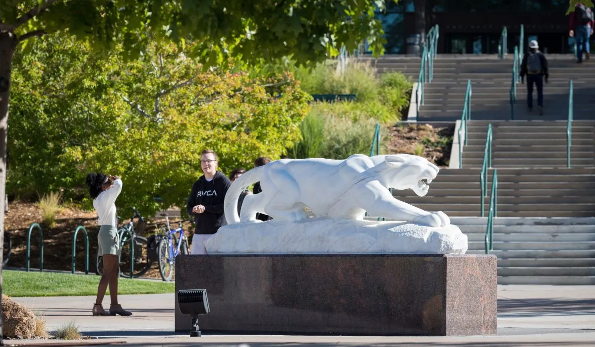 students walking past the Mountain Lion Statue on UCCS campus